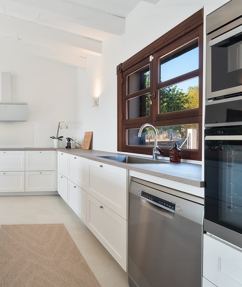 Cocina con muebles blancos, encimeras de piedra y marcos de madera bajo techos abovedados de madera blanca.