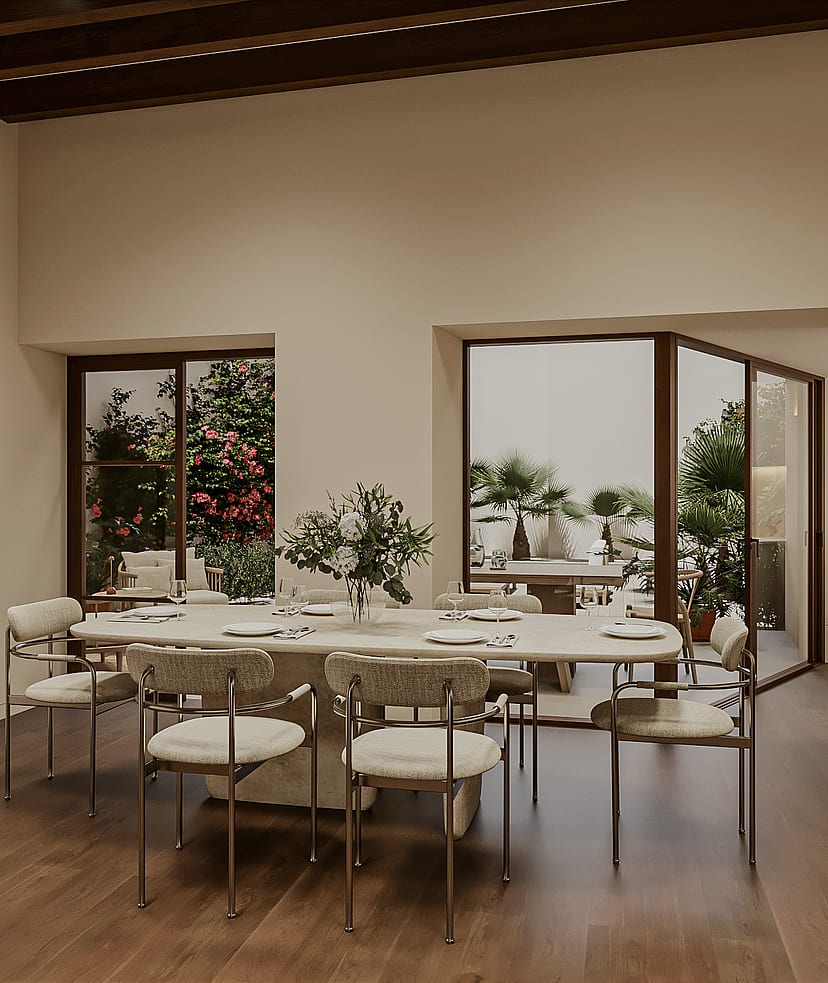 Dining table with eight chairs beside large windows and glazed doors overlooking a planted garden with bougainvillea and palms.