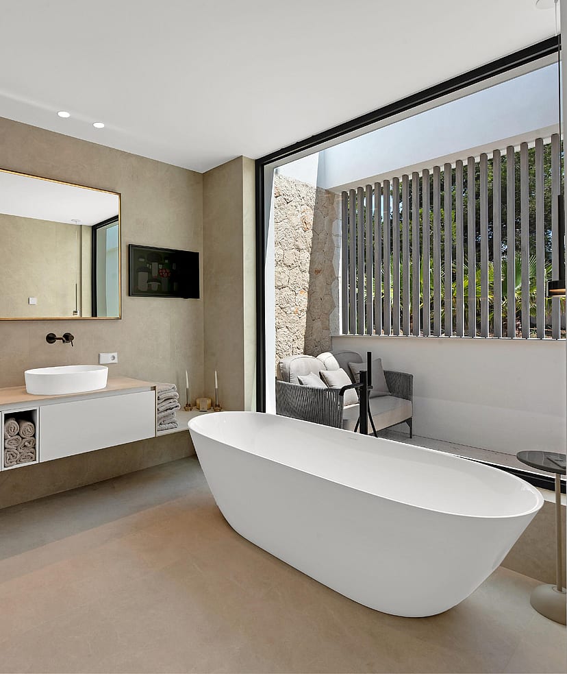 Spa-style bathroom with freestanding white bath, double vessel sinks, stone wall cladding and glazed opening to private terrace