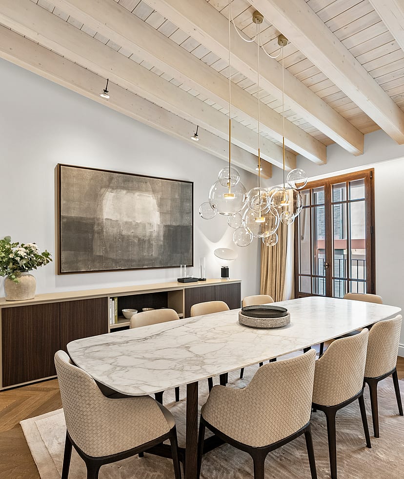Contemporary dining room featuring a white marble table, upholstered chairs, and exposed white-washed ceiling beams.