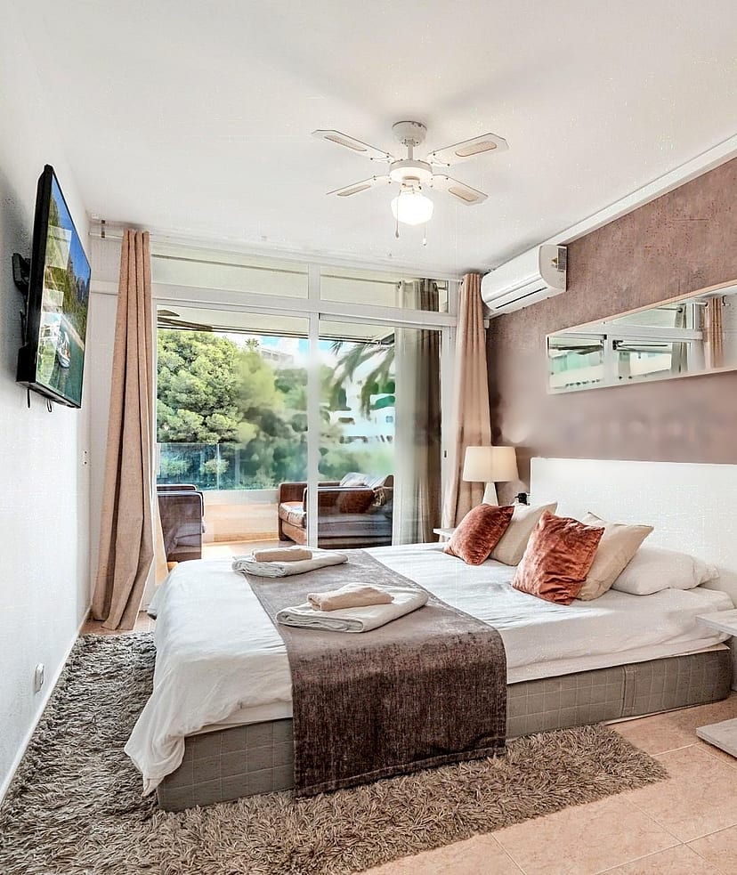 A modern bedroom featuring a large bed with neutral linens, a textured terracotta feature wall, and glass sliding doors leading to a private terrace.