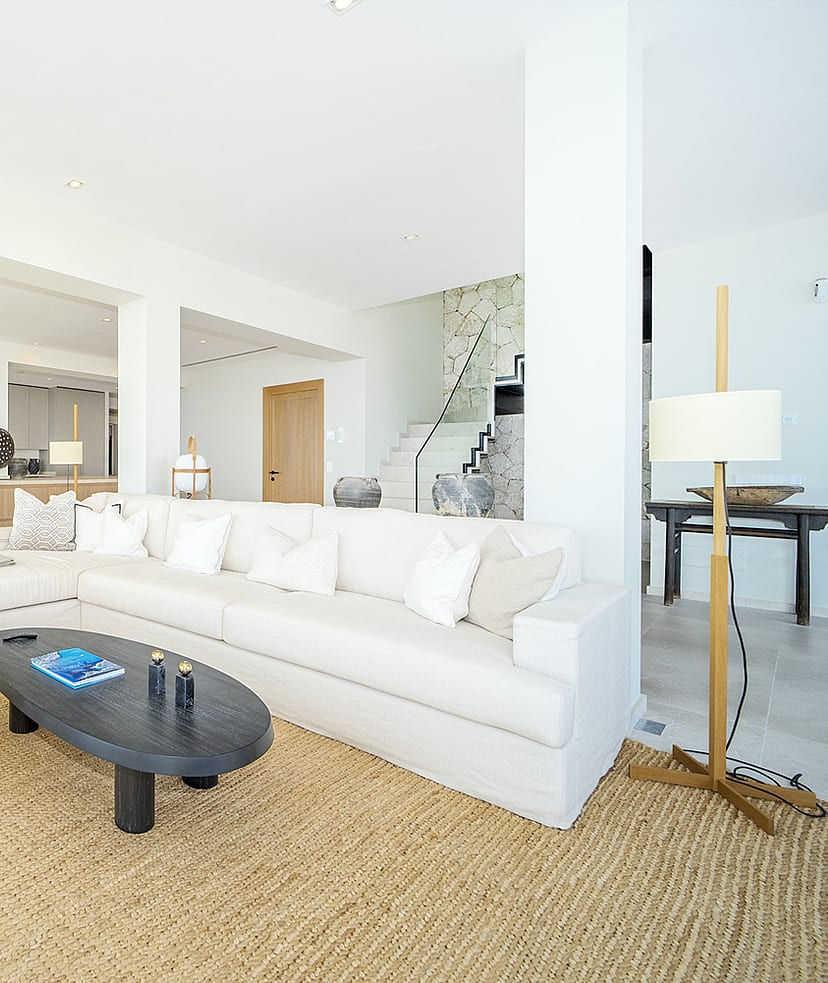 Bright open-plan living room in Illetas with white sectional sofa, oval coffee table, and a large textured jute rug.