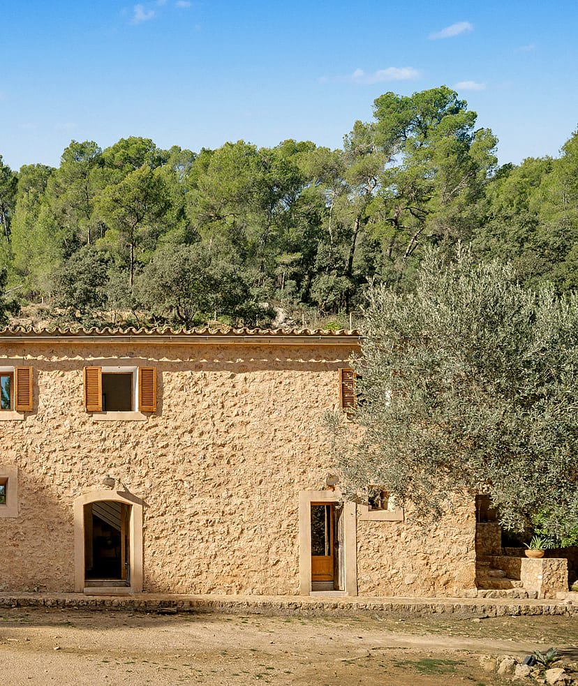Two-storey stone finca façade with wooden shutters and dry-stone walls