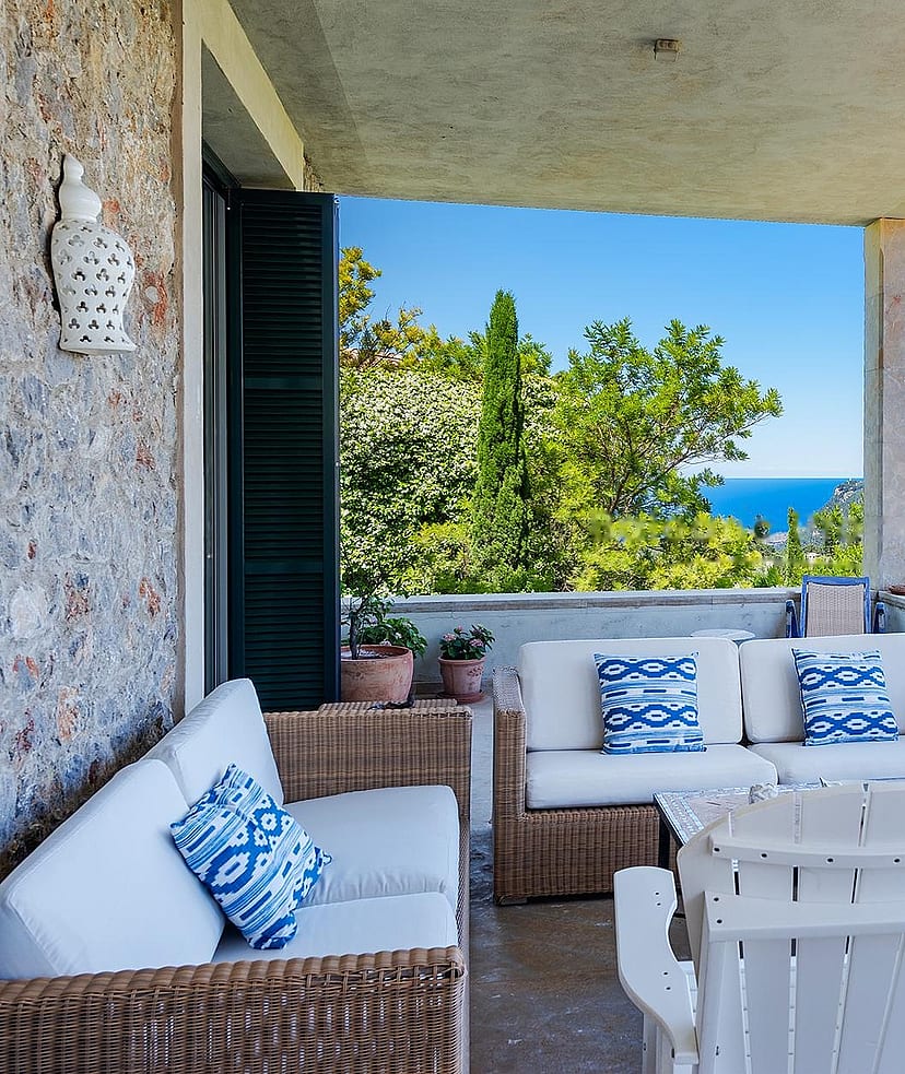 Large covered terrace with fireplace, multiple seating zones, and uninterrupted view across forested valley to distant mountains