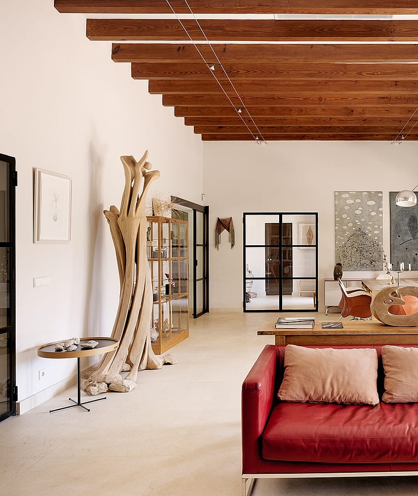 A spacious living room with high beamed ceilings, red leather sofa, and white walls in a Finca-style home.