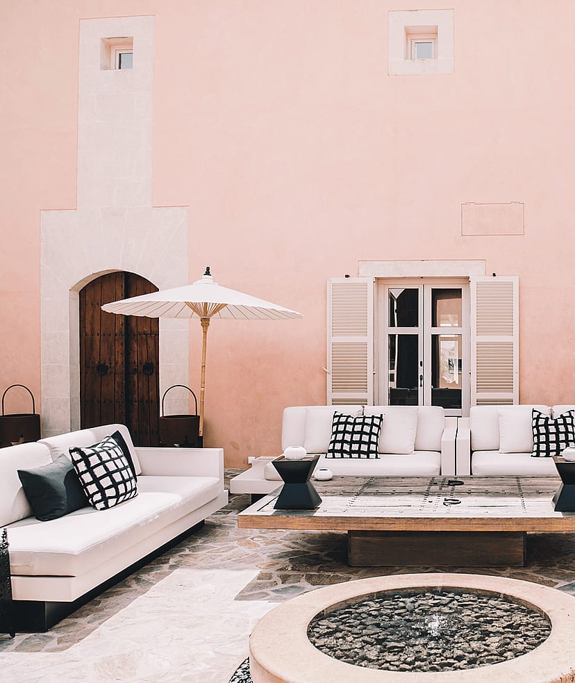 Outdoor courtyard of a Finca with pink plaster walls, white sofas, and stone flooring.