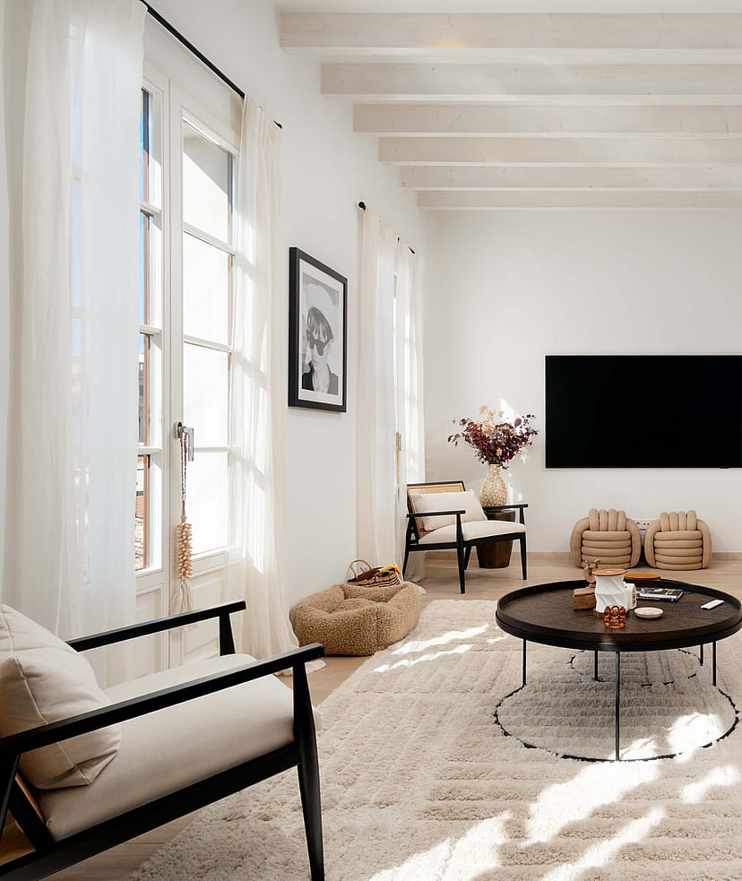 Living room with black cane armchairs, a cream linen sofa, black round coffee tables and framed black and white photography.