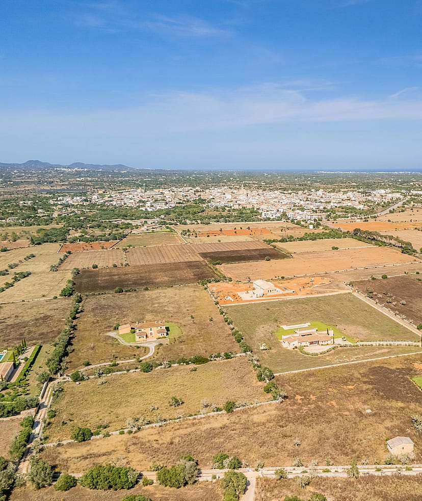 High-altitude aerial view of rural Mallorcan landscape near Santanyí, featuring sparse vegetation and distant town buildings.