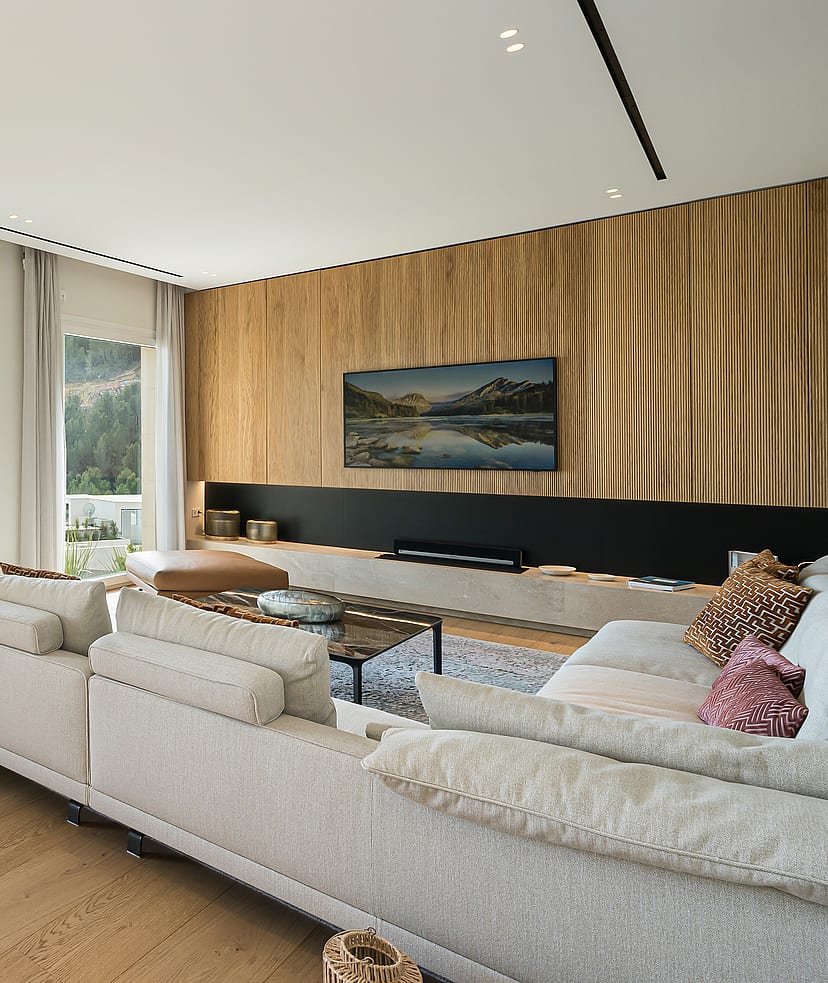 Spacious living room with beige sofa, wooden flooring, and floor-to-ceiling glass doors opening to a stone-railed terrace.