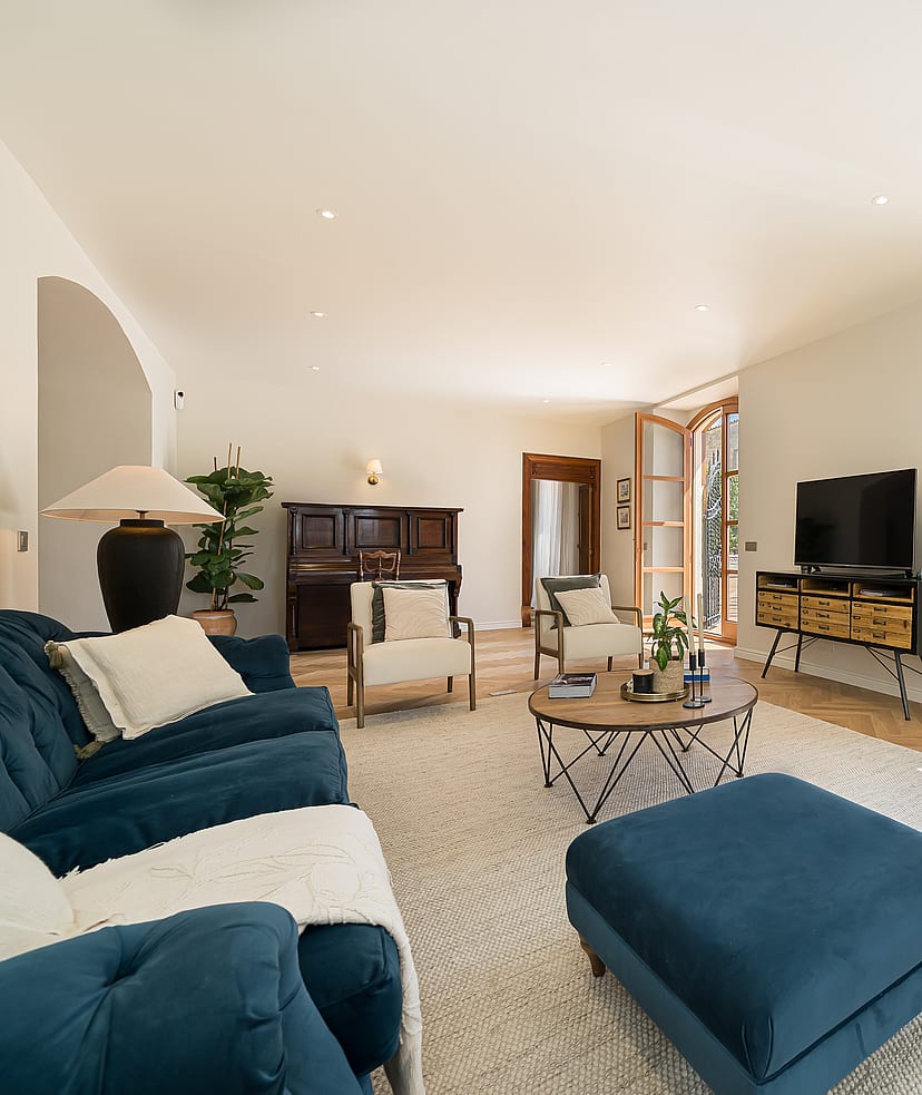 Living area featuring blue velvet tufted sofas, light herringbone wood floors, a dark piano, and arched patio doors.