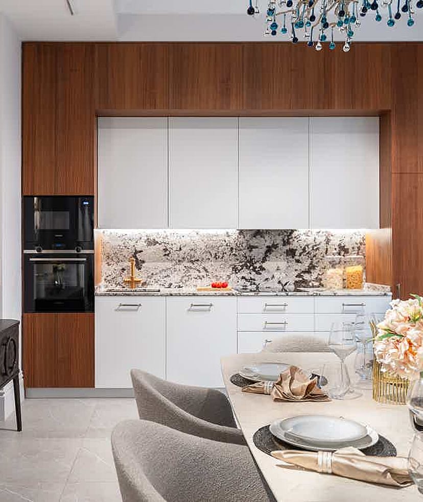 Modern kitchen with white cabinets, dark wood trim, and a patterned marble backsplash. Includes a side console and dining table.