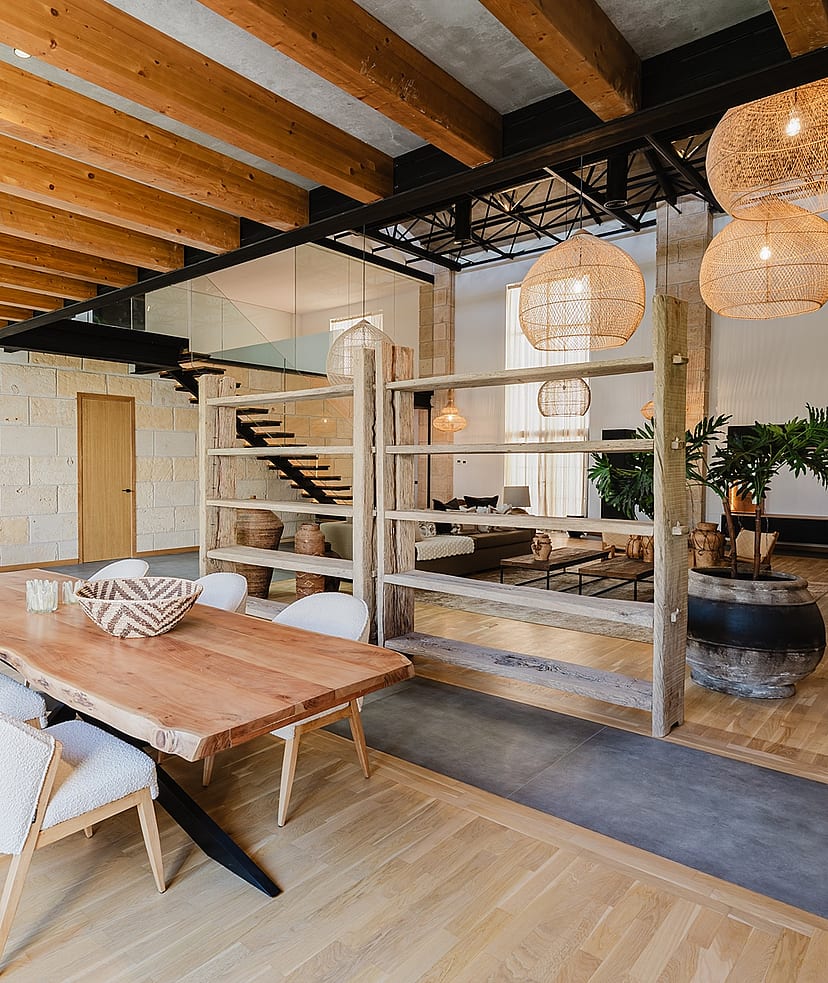 Dining room with a live-edge wooden table, wicker pendant lights, and exposed wooden ceiling beams in a loft-style apartment.