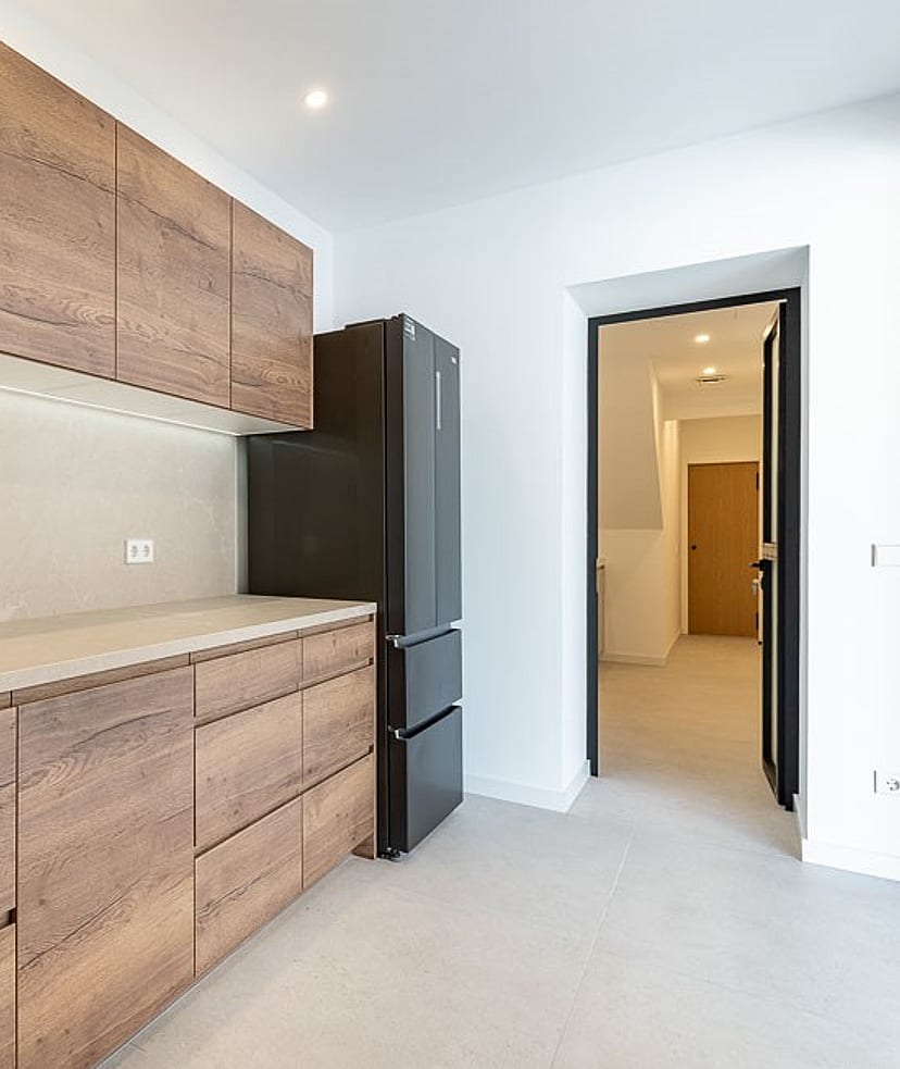 A modern kitchen in a townhouse features horizontal wood-grain cabinets, a matte black faucet, and a stone backsplash.