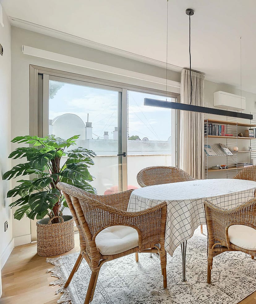 A bright dining area with a round table, wicker chairs, and large glass sliding doors opening onto a terrace with sea views.