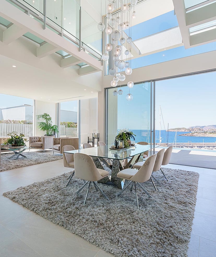 Double-height living and dining space with floor-to-ceiling sliding glass doors opening to a coastal view.