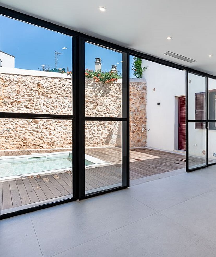 Modern open-plan living room with large floor-to-ceiling sliding glass doors opening onto a stone-walled terrace with a plunge pool.