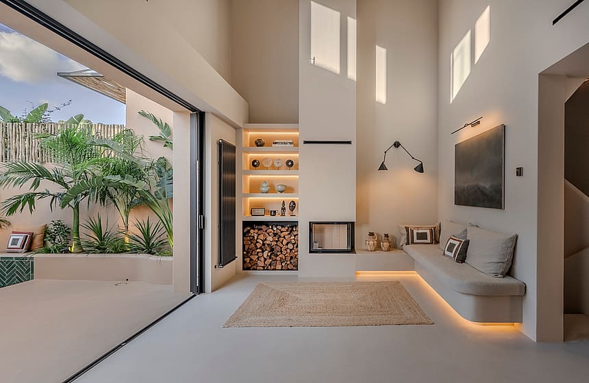 Double-height living area featuring a built-in sofa, modern fireplace, and glass doors opening to a tropical patio.