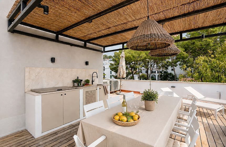 Outdoor dining terrace featuring a wicker-covered pergola, a built-in stone kitchen station, and a long dining table.
