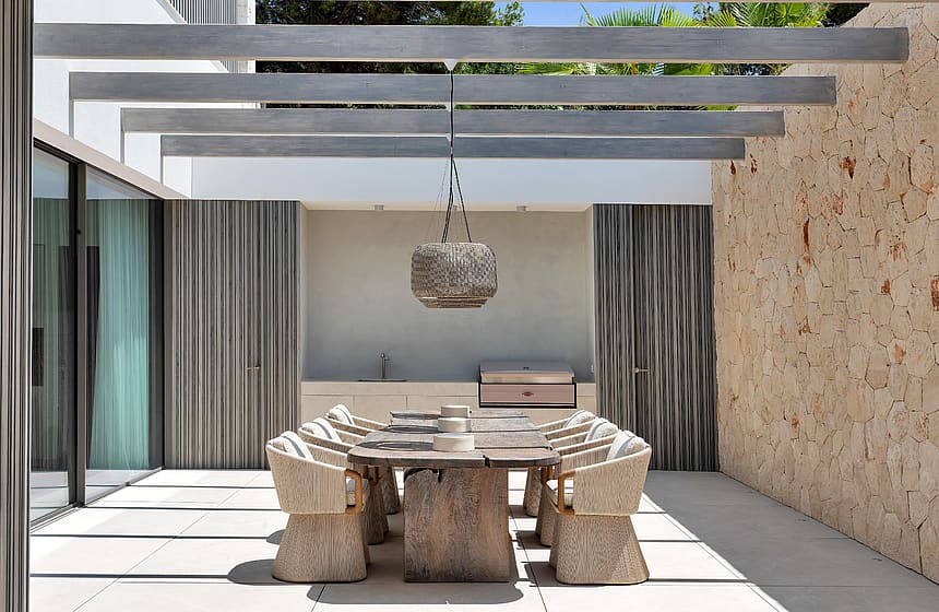 Covered outdoor dining area with exposed beam pergola, Mallorcan stone wall and wicker pendant lights