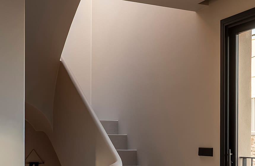 Modern staircase with seamless microcement finish, sculptural handrail, and black-framed door in a Genova townhouse.