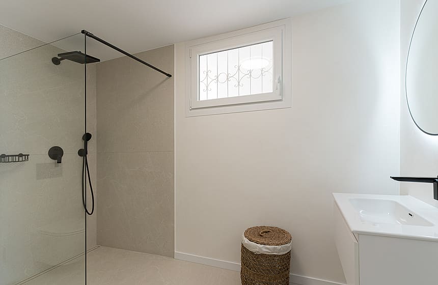 A contemporary walk-in shower featuring a glass partition, matte black rain shower head, and large-format sand-colored tiles.