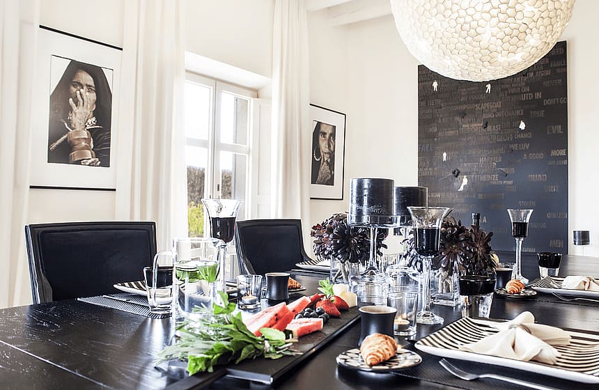 A formal dining room interior with a black lacquered table, black dining chairs, a large textured spherical pendant light, and framed monochrome photography on white walls.