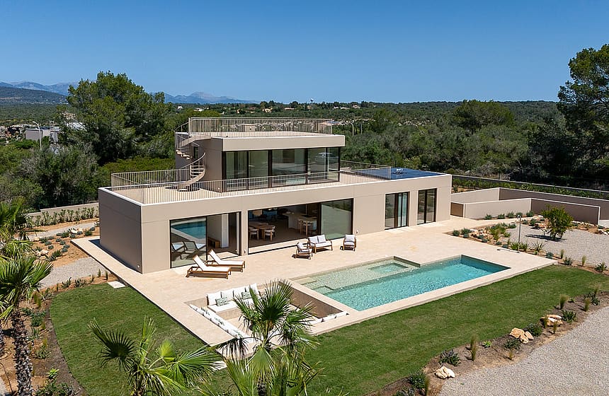 Aerial view of a modern beige villa in Son Gual featuring a rectangular swimming pool, terrace, and mountain backdrop.
