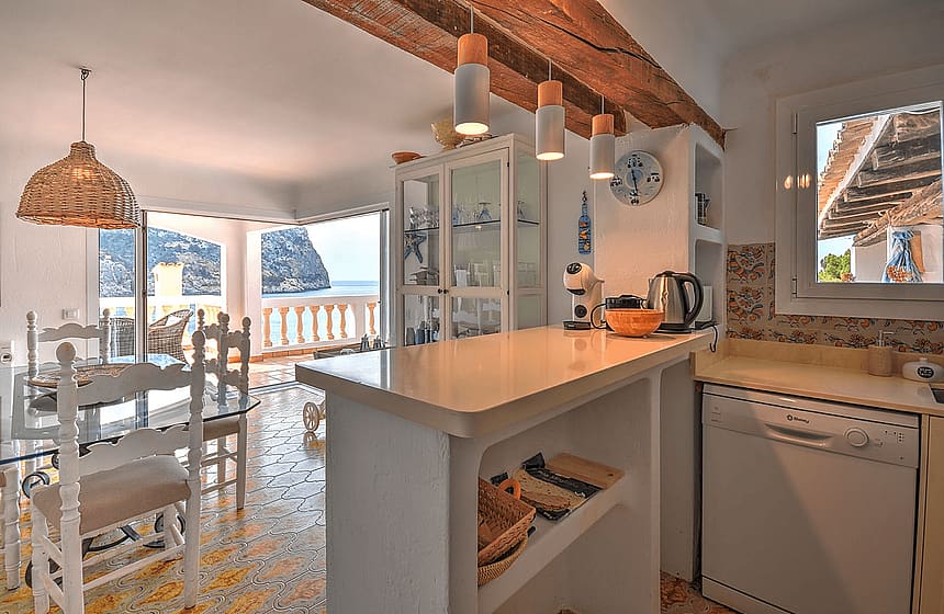 Kitchen and dining area with white cabinets, patterned tiled floor, and views of the Mediterranean coastline.