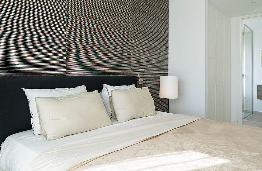 Close-up of a king-size bed featuring a dark upholstered headboard and a wall panel with horizontal ridged texture.