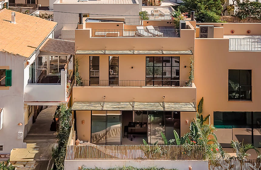 Exterior view of a multi-level townhouse in Genova featuring a beige stucco facade, large glass sliding doors, and a rooftop terrace.