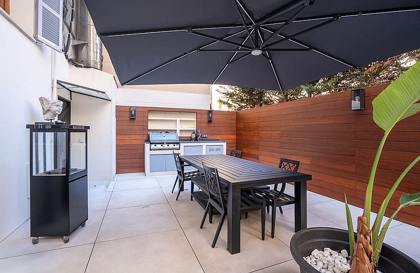 A private outdoor terrace in Palma featuring a dining table, black chairs, a large charcoal umbrella, and a built-in grill.