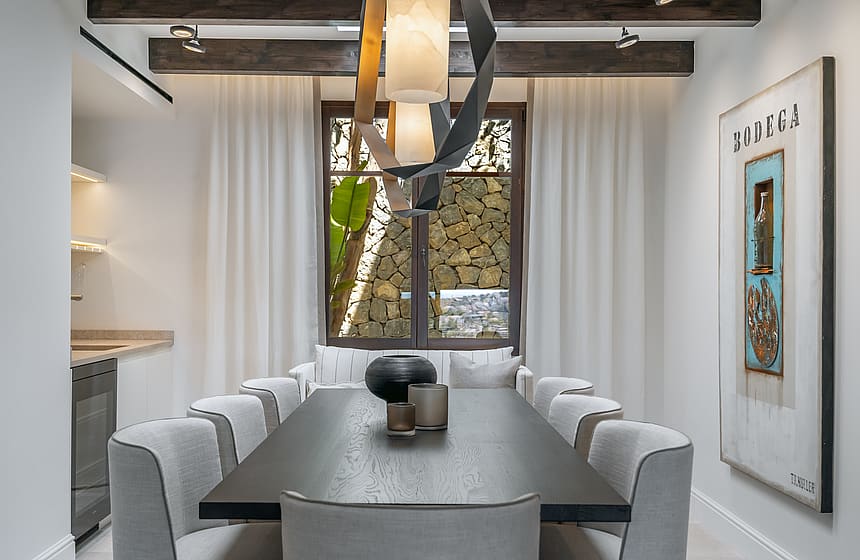 Dining area with a dark wood table, grey chairs, exposed ceiling beams, and a sculptural light fixture.