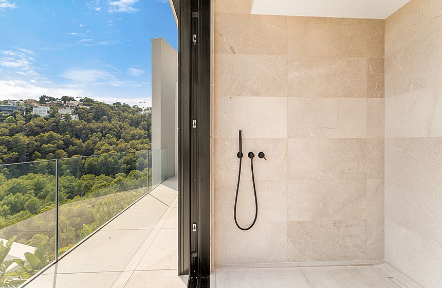 A modern bathroom featuring a walk-in shower with matte black fixtures and a glass-paneled terrace overlooking a green hillside.
