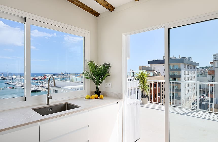 Modern kitchen corner with white cabinets and stone countertop, featuring large sliding glass doors opening to a balcony.