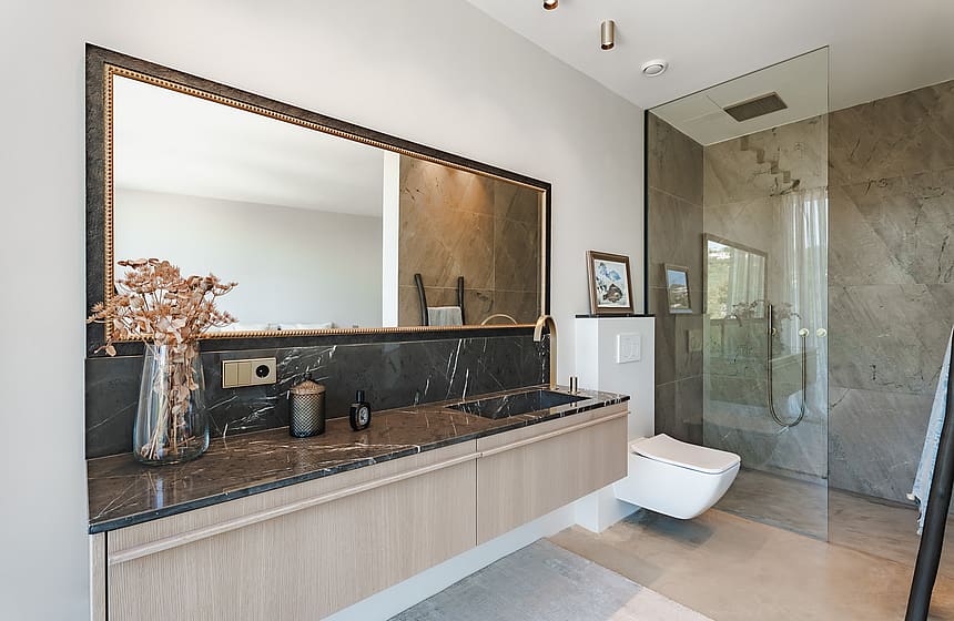 Modern bathroom featuring a floating oak vanity with a dark stone top, walk-in glass shower, and a large framed mirror.
