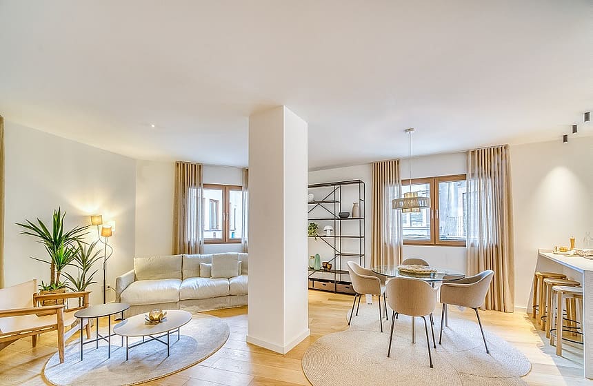 An open-plan living and dining room with oak floors, a central structural column, and neutral beige furniture.