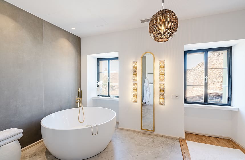 Modern bathroom featuring a white oval freestanding bathtub against a grey accent wall and two windows with mountain views.