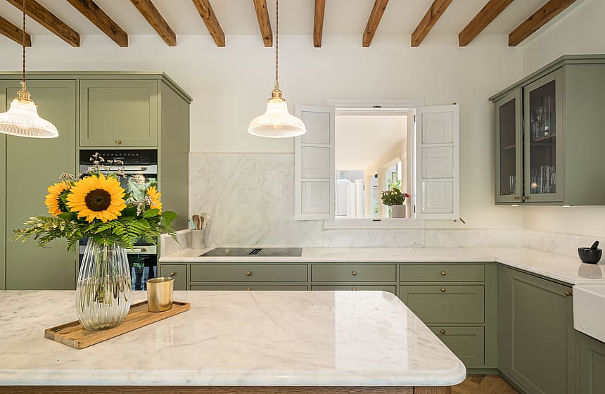 Contemporary kitchen featuring sage green cabinets, white marble countertops, exposed ceiling beams, and pendant lighting.