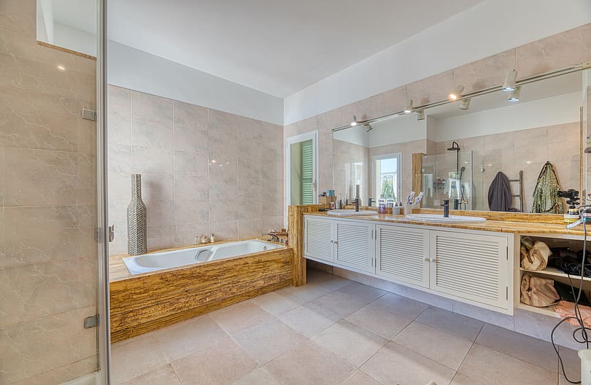 Master bathroom featuring a stone-clad soaking tub, double vanity with white cabinetry, and large wall-mounted mirrors.
