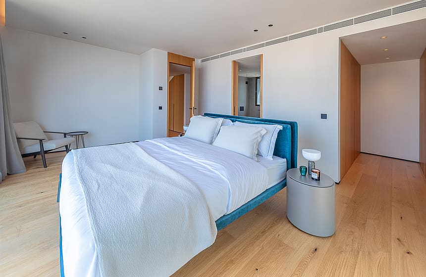 Bright bedroom featuring a teal upholstered bed, light oak flooring, and wood-paneled walk-in closet entrance.