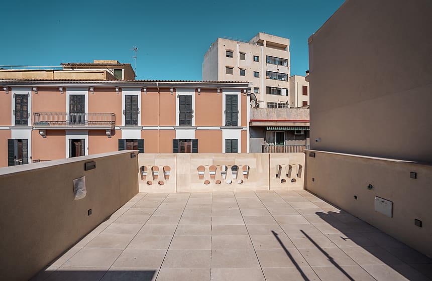 A rooftop terrace featuring square stone tiles and an ornate balustrade against a backdrop of terracotta townhouses.