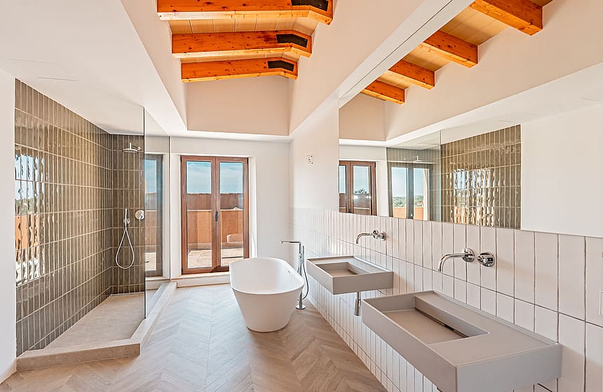 Modern bathroom featuring double concrete vanity, freestanding bathtub, walk-in shower, and exposed wood ceiling beams.