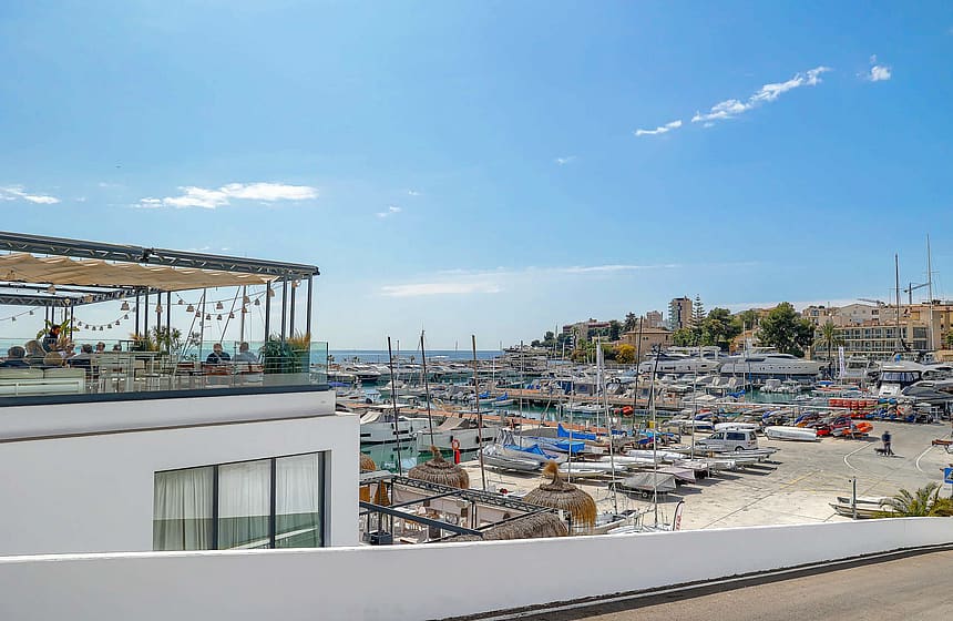 An elevated view overlooking a busy marina and harbor with small boats, viewed from a white modern building terrace.