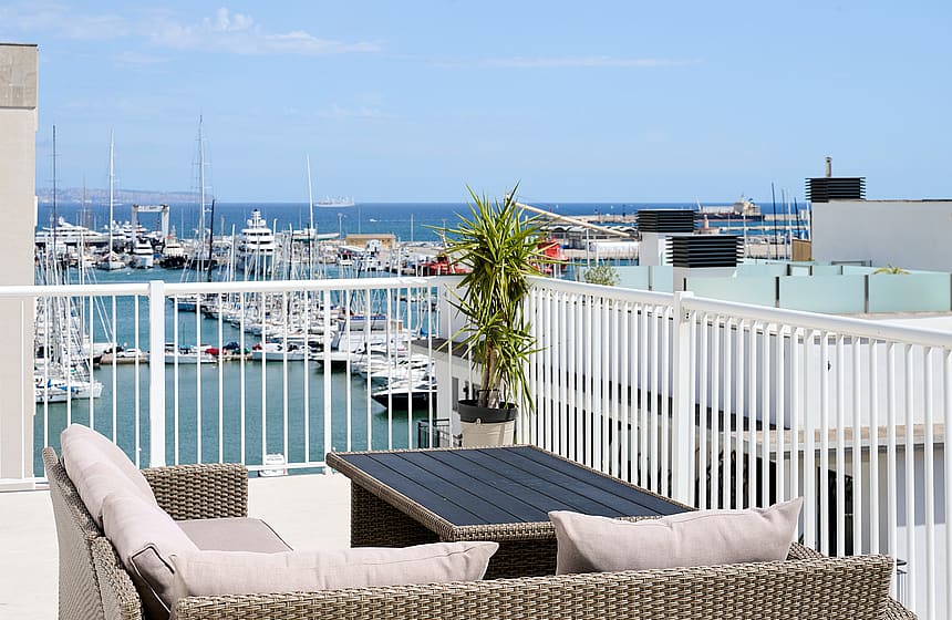 A rooftop terrace with wicker furniture overlooking a marina filled with boats under a clear blue sky in Santa Catalina.