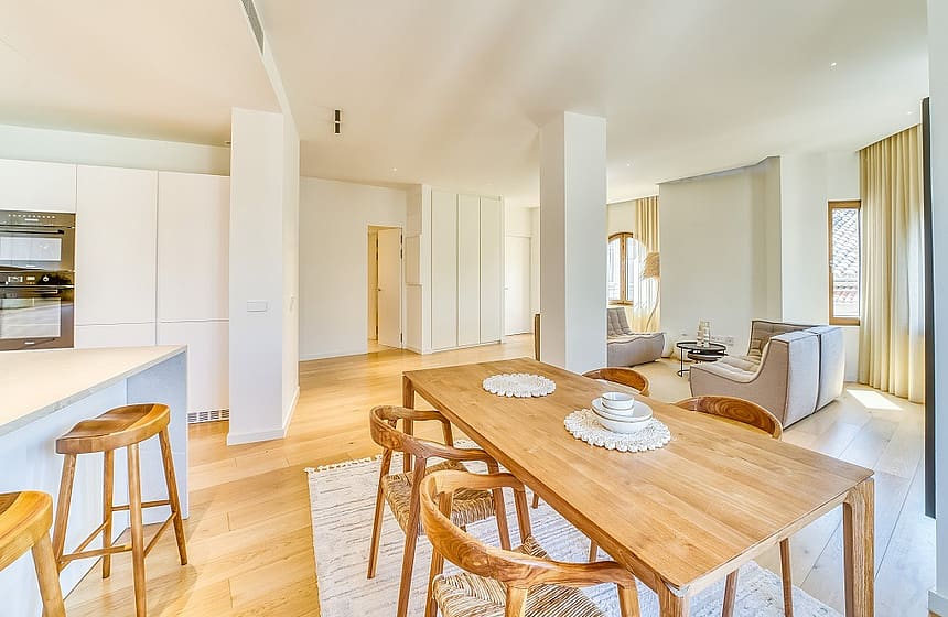 Open-plan room featuring a light wood dining table with curved wooden chairs and a minimalist kitchen island with bar stools.
