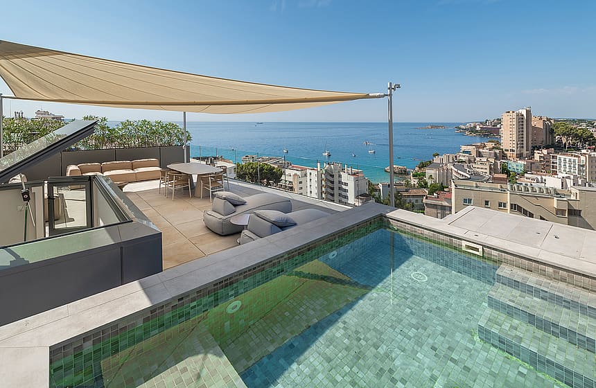 Elevated view of a penthouse terrace featuring a tiled plunge pool, outdoor dining area under a shade sail, and sea horizon.