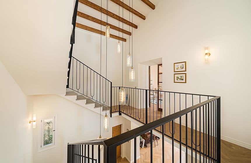Modern staircase featuring black iron railings, exposed wooden beams, and a cluster of cylindrical glass pendant lights.