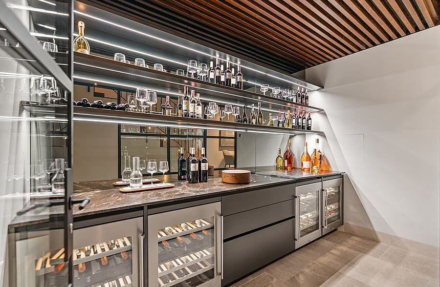 Dark-toned wine cellar with backlit glass shelves, integrated temperature-controlled fridges, and a marble workspace.