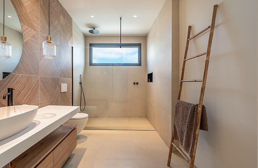 A contemporary bathroom featuring a white vessel sink on a floating wood vanity, a textured bronze accent wall, and a large walk-in shower area with a bamboo towel ladder.