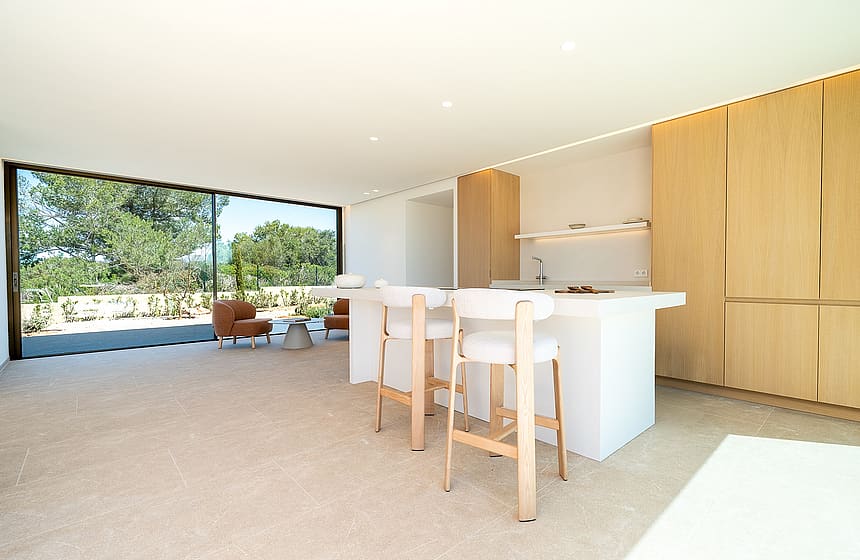 Modern open-plan kitchen with a white island, wooden cabinetry, and large sliding glass doors overlooking mountain scenery.